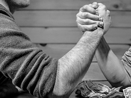 Two gentlemen arm wrestling on a table covered with money, signifying that if you do things correctly in the first place, you won't need to struggle.