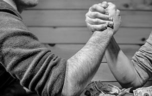 Two gentlemen arm wrestling on a table covered with money, signifying that if you do things correctly in the first place, you won't need to struggle.