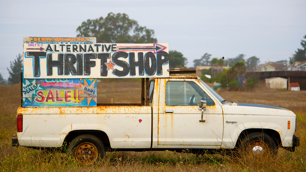 Rusty pickup truck with signs that say alternative thrift shop and super deals, signifying that the quality you receive equates to how much you spend.