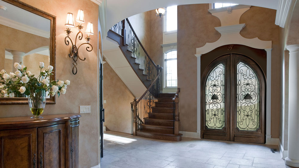 A well appointed traditional interior entryway highlighted by an ornate iron and wood double entry door.