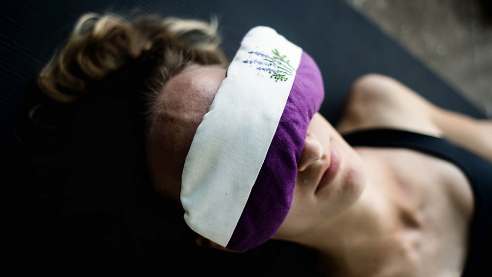 Meditating woman lying on the floor with a lavender mask over her eyes, signifying the importance of insulation and dampened sound in the room