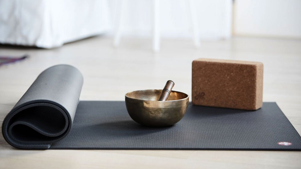 A cork block and Tibetan singing bowl on a dark gray yoga mat, shows the importance of planning for storage space to put tools in your yoga room.