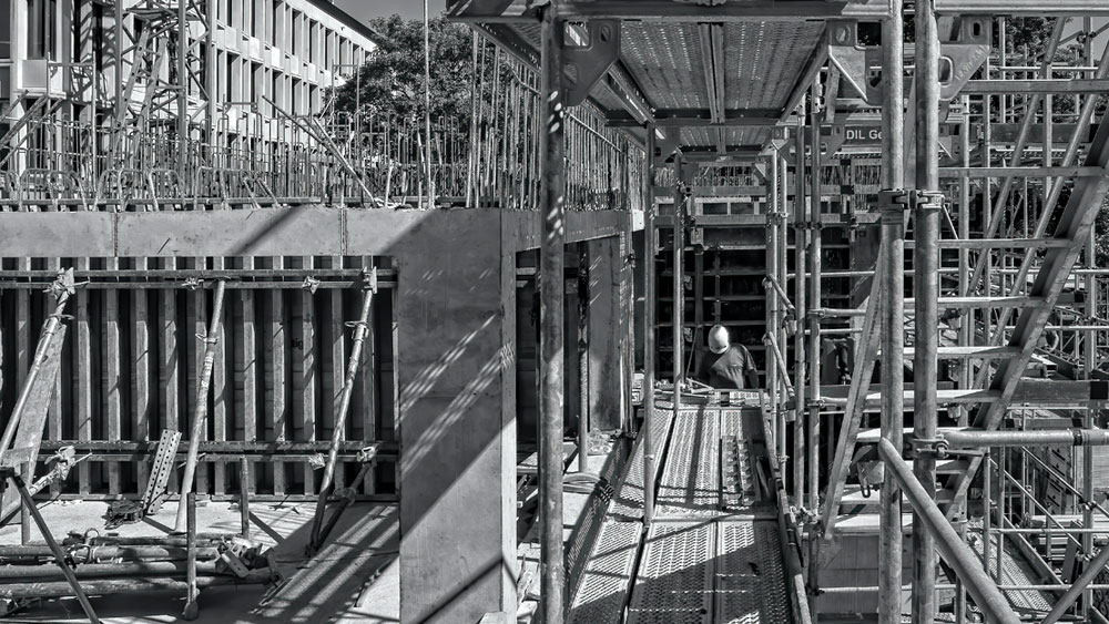 Black and white image of construction of the foundation of a commercial building surrounded by scaffolding, signifying the slowly rising ABI scores.