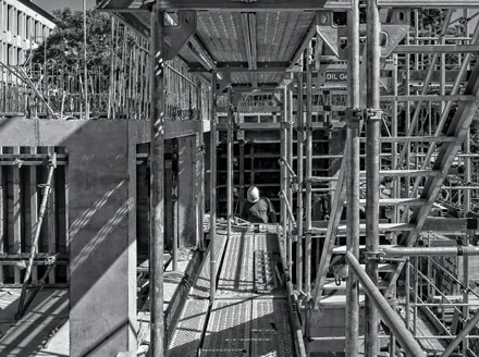 Black and white image of construction of the foundation of a commercial building surrounded by scaffolding, signifying the slowly rising ABI scores.