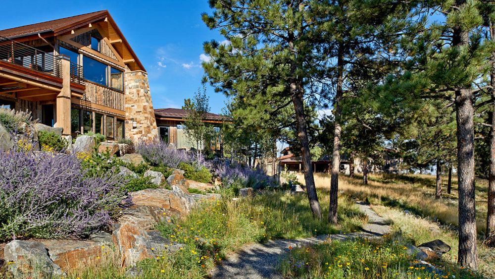 Stone house in Denver surrounded by native trees, large boulders, and xeriscape with a gray gravel pathway