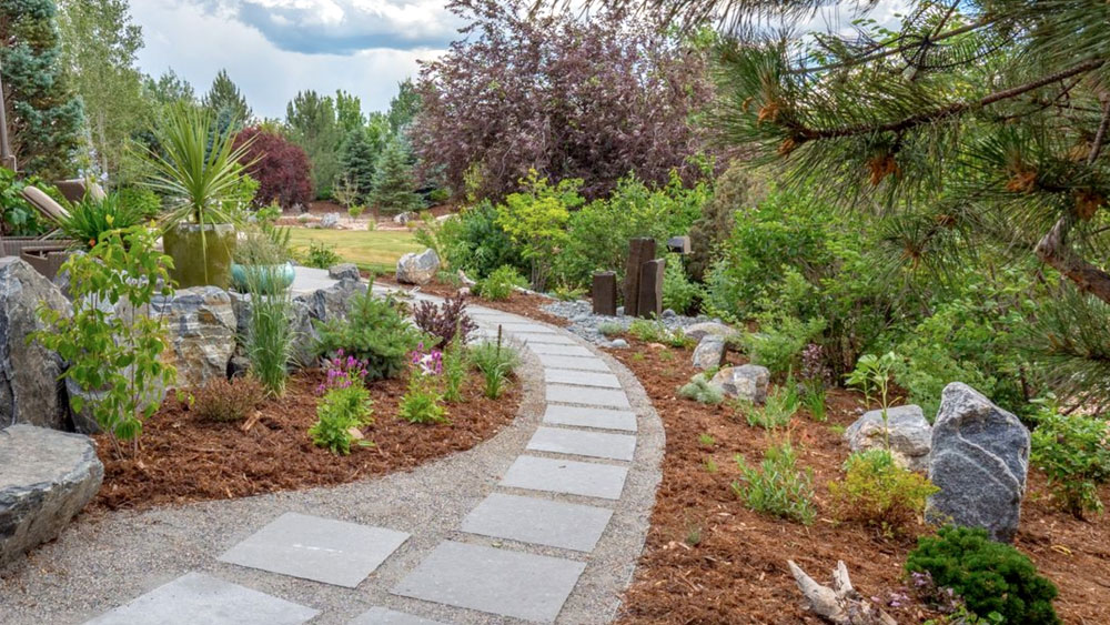 Gray gravel and square paver pathway surrounded by large decorative boulders and wood mulched xeriscape