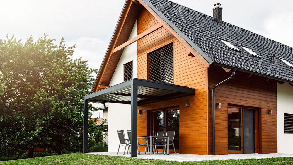 Passive House Design A modern passive house with slatted sun shades, black solar roof tiles, wood siding, and a metal overhang to shade the sliding glass door.