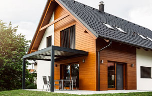 Passive House Design A modern passive house with slatted sun shades, black solar roof tiles, wood siding, and a metal overhang to shade the sliding glass door.