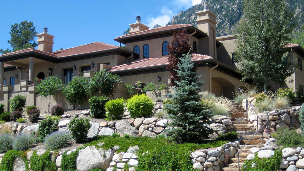 A terraced yard with native xeriscape plantings and large boulders in front of a Spanish revival home in Colorado