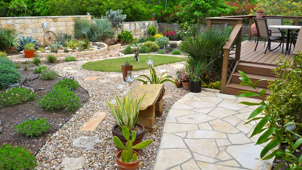 Raised wooden deck surrounded by pebble stone pathways and mulched beds with water-saving plants, signifying the many design options in xeriscaping