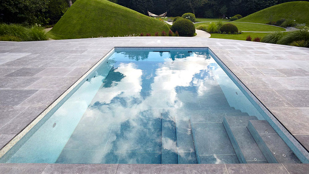 Rectangular pool with tile pool deck and moveable tile floor that serves as a pool cover when closed with green pasture hills in the background