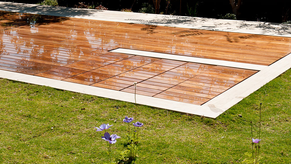 A moveable floor teak pool cover that is closed to create a wooden deck, concealing the rectangular pool beneath