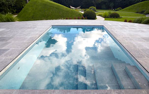 Rectangular pool with tile pool deck and moveable tile floor that serves as a pool cover when closed with green pasture hills in the background