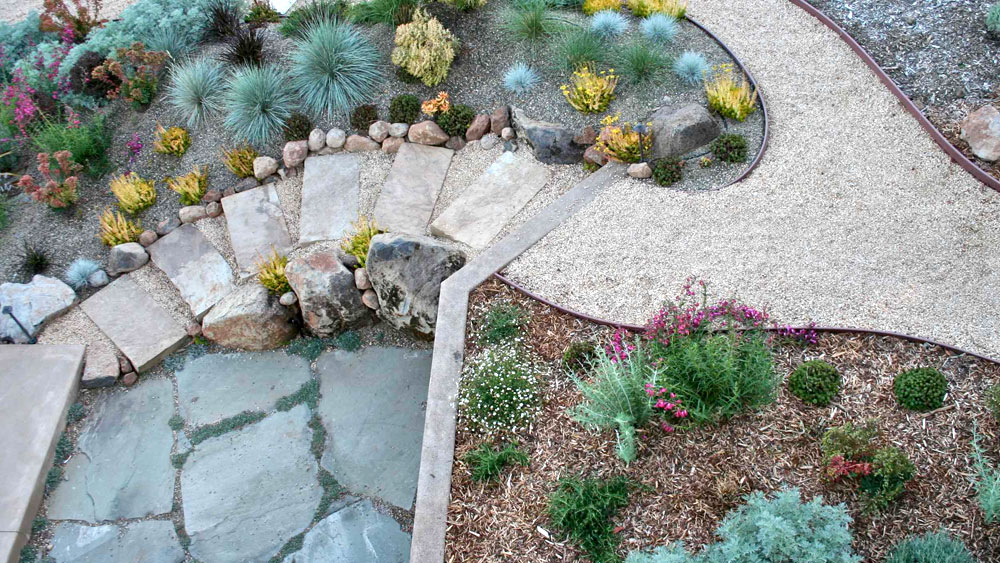 Xeriscaped sloping pathway of crushed gravel between bark and rock mulched xeric beds