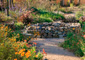 Crushed granite pathway through lush xeriscape with colorful blooming wildflowers and a stone well in the center