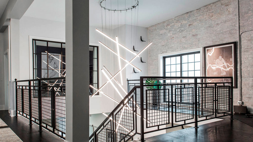 The foyer of a rehabilitated firehouse features a modern and sleek Monorail Cirrus Float R1 Rectangular Suspension chandelier from PureEdge Lighting.