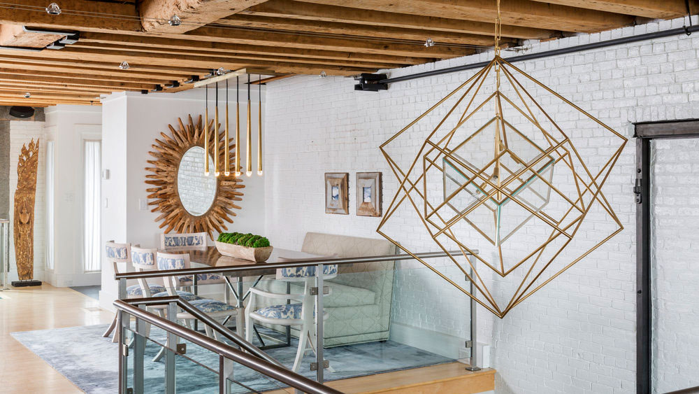 A gold and glass Cubist chandelier by Kelly Wearstler for Visual Comfort hanging in the 2-story foyer of a modern loft from an exposed wood joist.