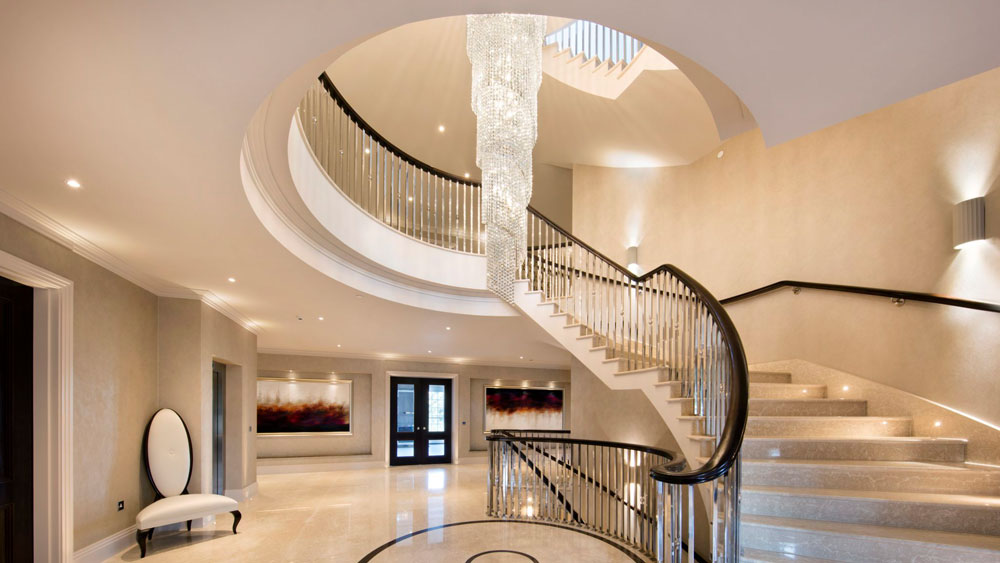 A spiral staircase in a grand entryway illuminated and accentuated by a draping spiral crystal chandelier, wall sconces, and recessed lights.