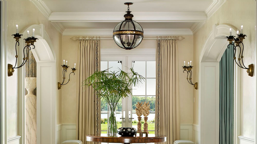 Traditionally decorated foyer interior with metal and glass orb pendant lights and coordinating candelabra wall sconces.