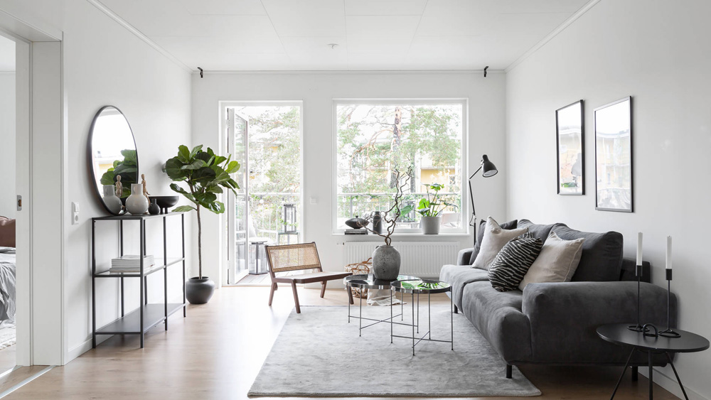 A BoKlok home's white living room, with a door that opens to the terrace and a large picture window, modern furniture and art from IKEA.