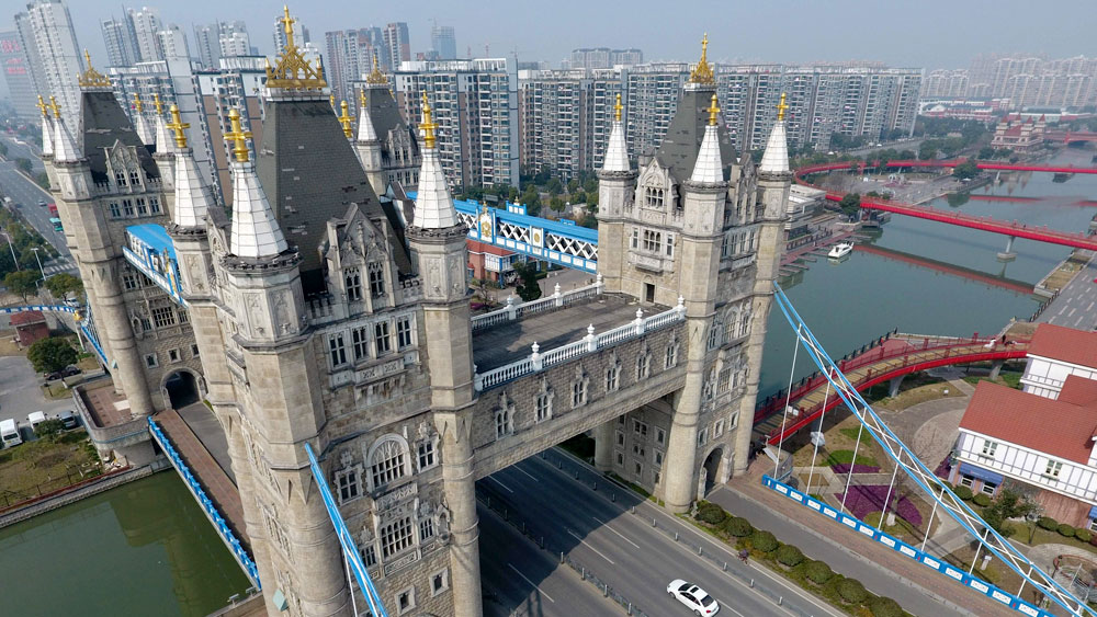 A replica of London's Tower Bridge in Suzhou, China shown with 4 turrets instead of the original 2 over a waterway with a cityscape in the background