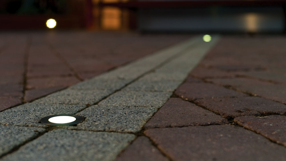 Night view of in-ground path lights leading up a residential driveway featuring WAC Lighting's Slim Recessed Luminaire.