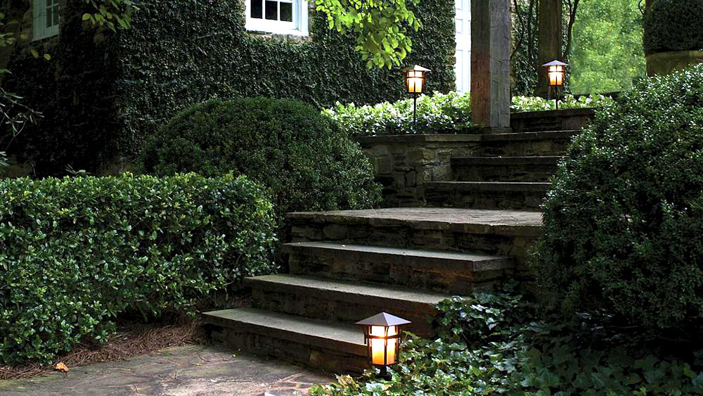 Photo of an ivy covered house and stone walkway, accented by the Hinkley Harbor post lantern path lights in a bronze finish.