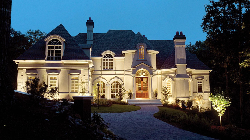 Evening exterior of a French traditional stucco home with wall-wash landscape lights from WAC Lighting.