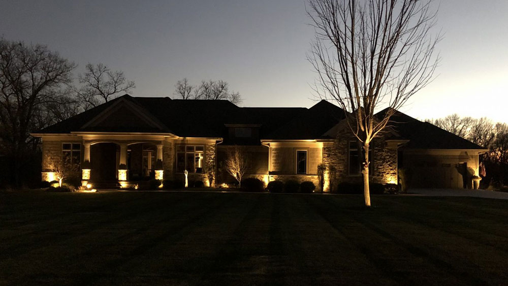 Exterior of a brick house at night with up-lighting that creates haunting shadows on the house