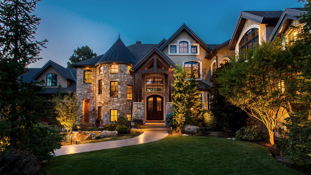 Stone and stucco estate exterior at night, lit by layered exterior lighting