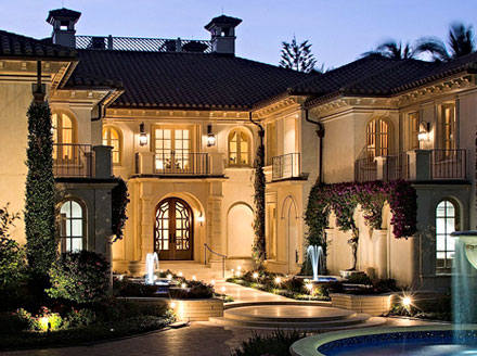 Evening exterior of stucco Mediterranean mansion in Naples, Florida with circular paver driveway surrounding a large fountain.