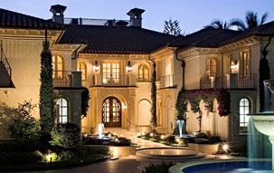 Evening exterior of stucco Mediterranean mansion in Naples, Florida with circular paver driveway surrounding a large fountain.