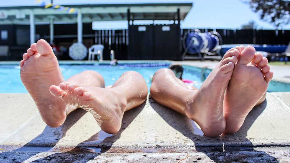 Feet of little kids sticking out of the side of a pool on a sunny day.