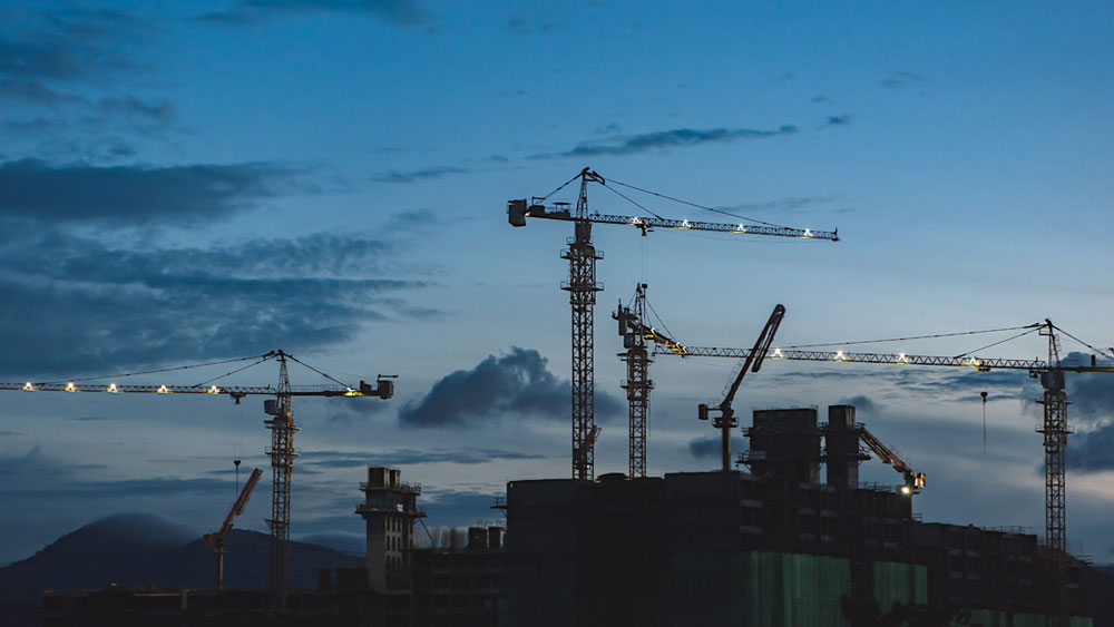 Multiple construction cranes lit up at dusk, signifying the slowdown in commercial construction activities since the onset of the pandemic.