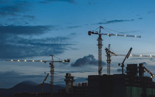 Multiple construction cranes lit up at dusk, signifying the slowdown in commercial construction activities since the onset of the pandemic.